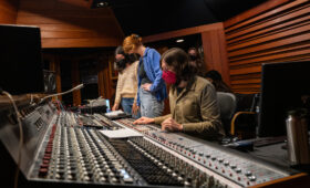 Photo of popular music students working around a professional mixing board at a sound studio.