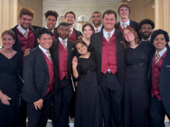 Photograph of college-aged choral singers in black concert attire smiling together inside a cathedral.
