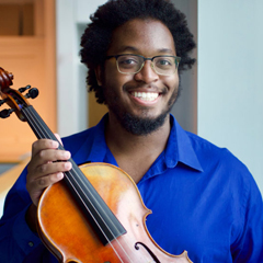 Photo of a viola student holding their instrument and smiling indoors.
