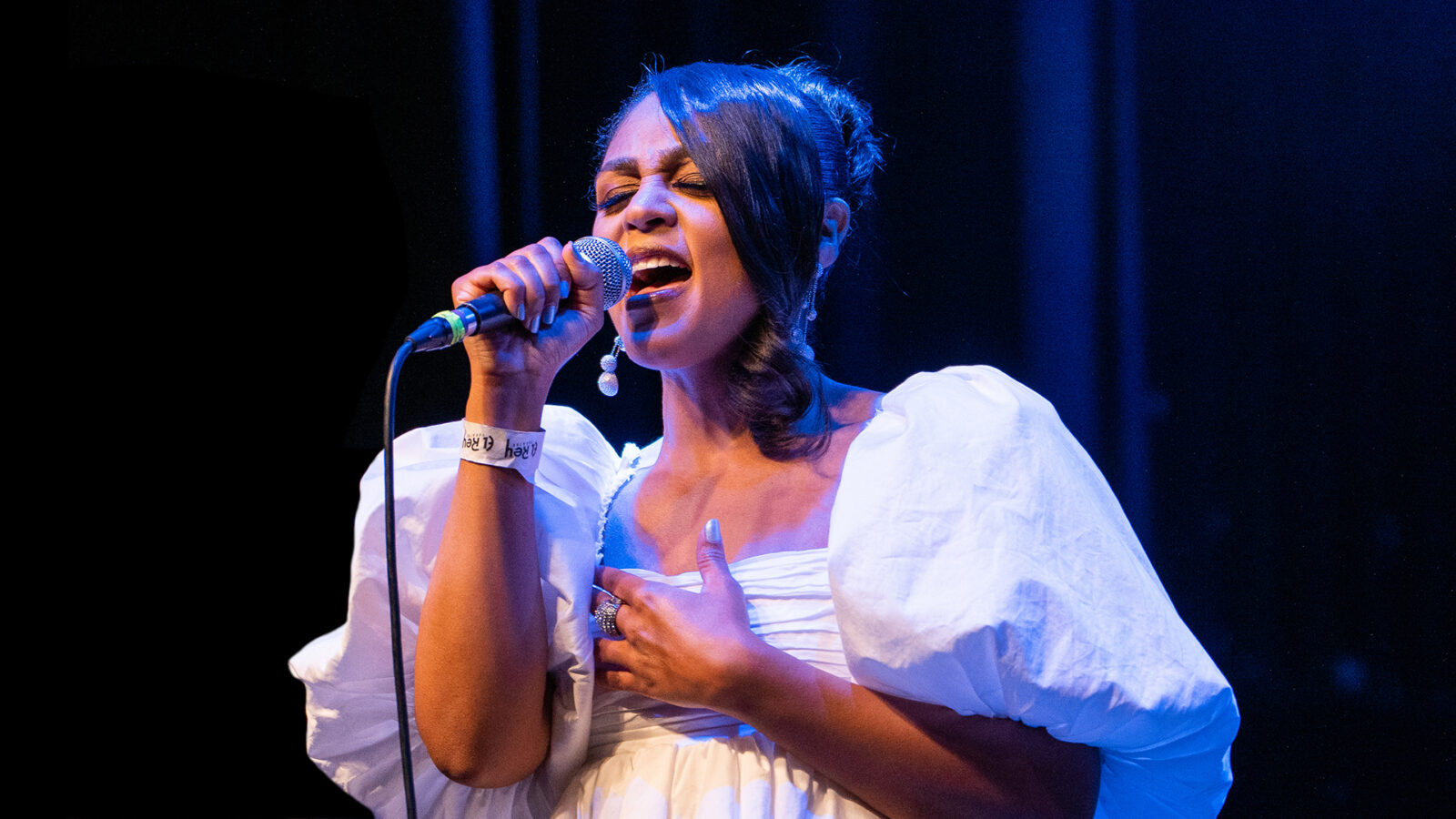 Photo of a popular music singer in white concert attire performs on stage holding a microphone. 