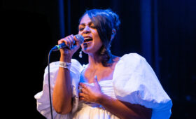 Photo of a popular music singer in white concert attire performs on stage holding a microphone.