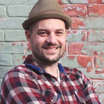 Photo of Eli Brueggemann smiling and wearing a hat.