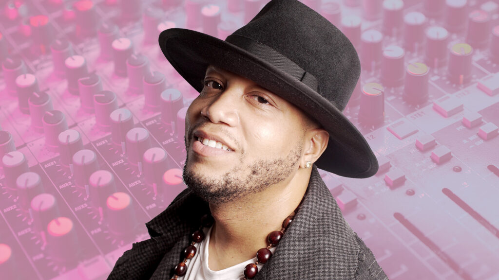 Photo of Andrae Alexander wearing a dark hat in front of a colorful photo of an audio mixing board.