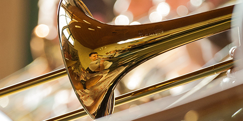 Photo of a performer's reflection in a trombone.