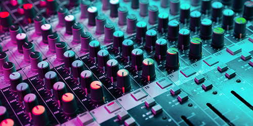 Photo of a mixing board under blue and purple light.