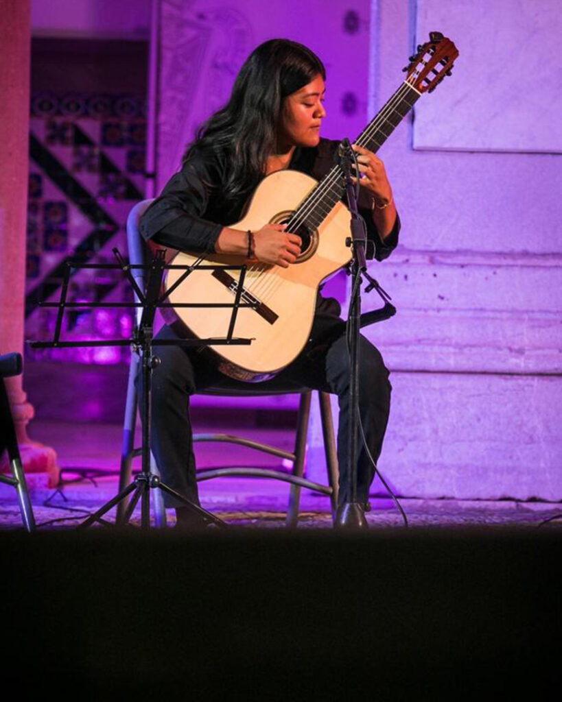 Photo of a classical guitarist playing their instrument on stage.