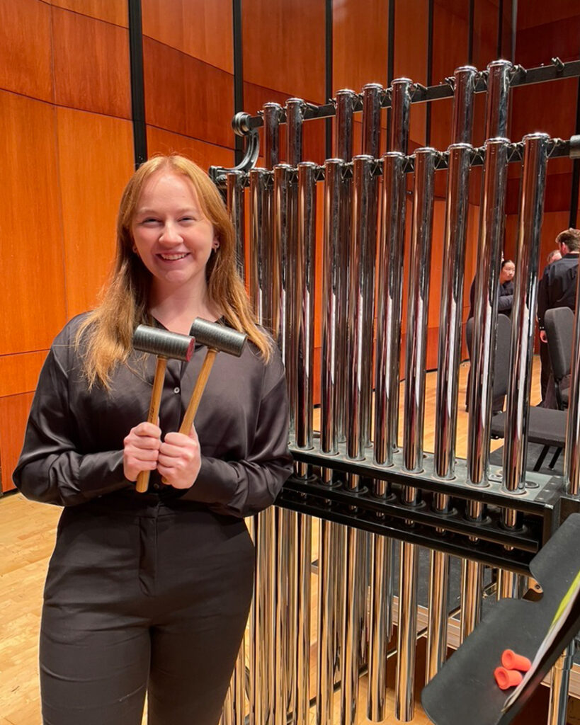 Photo of a percussionist posing with a set of tubular bells on a symphony concert stage.