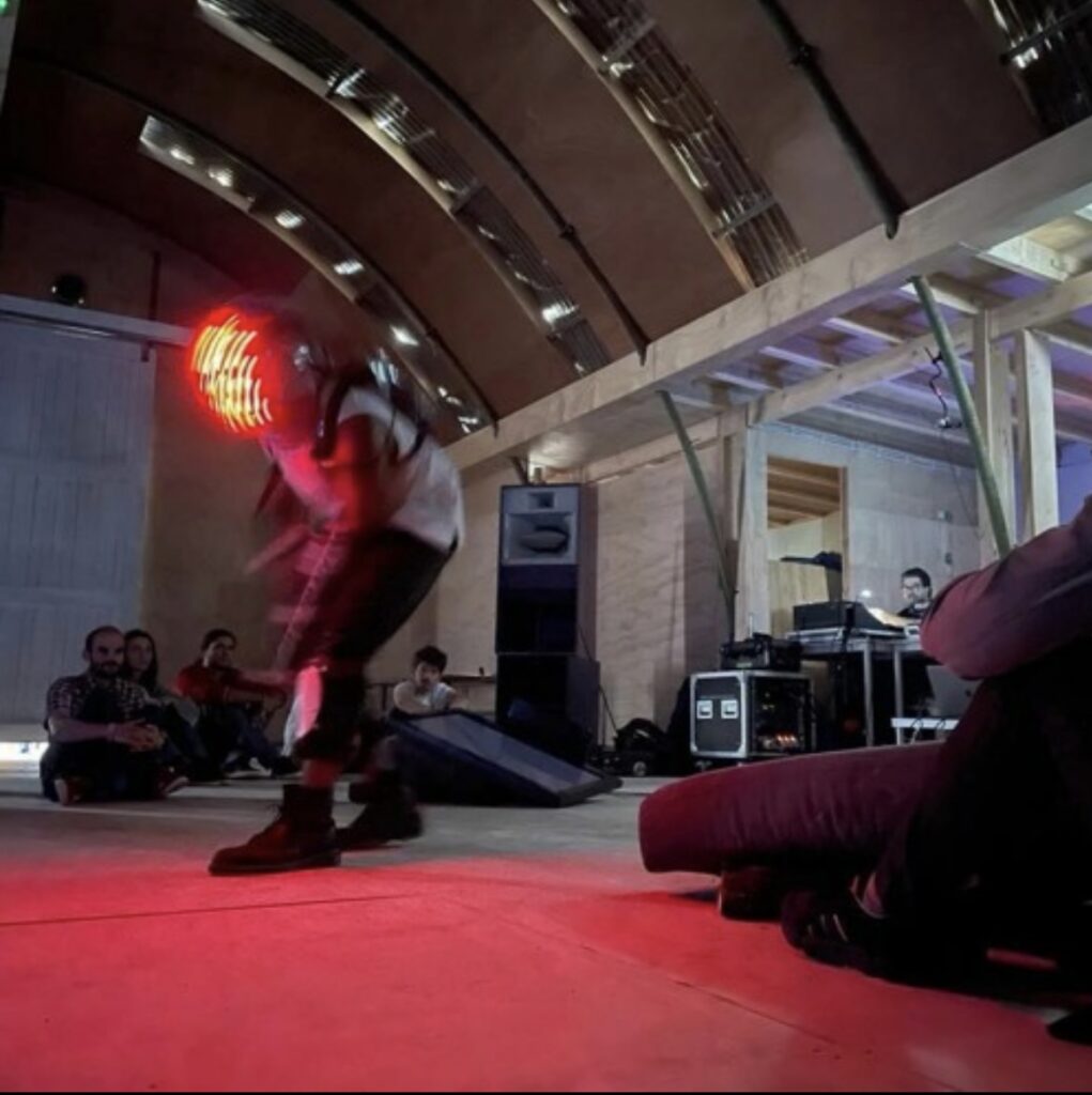 Photo of a music performer dancing in a electronic suit with a glowing red face mask.