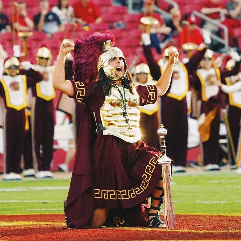 Photo of a drum major performing on a football field in gold Trojan armor.