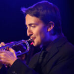 Photo of a trumpet player in purple stage light.