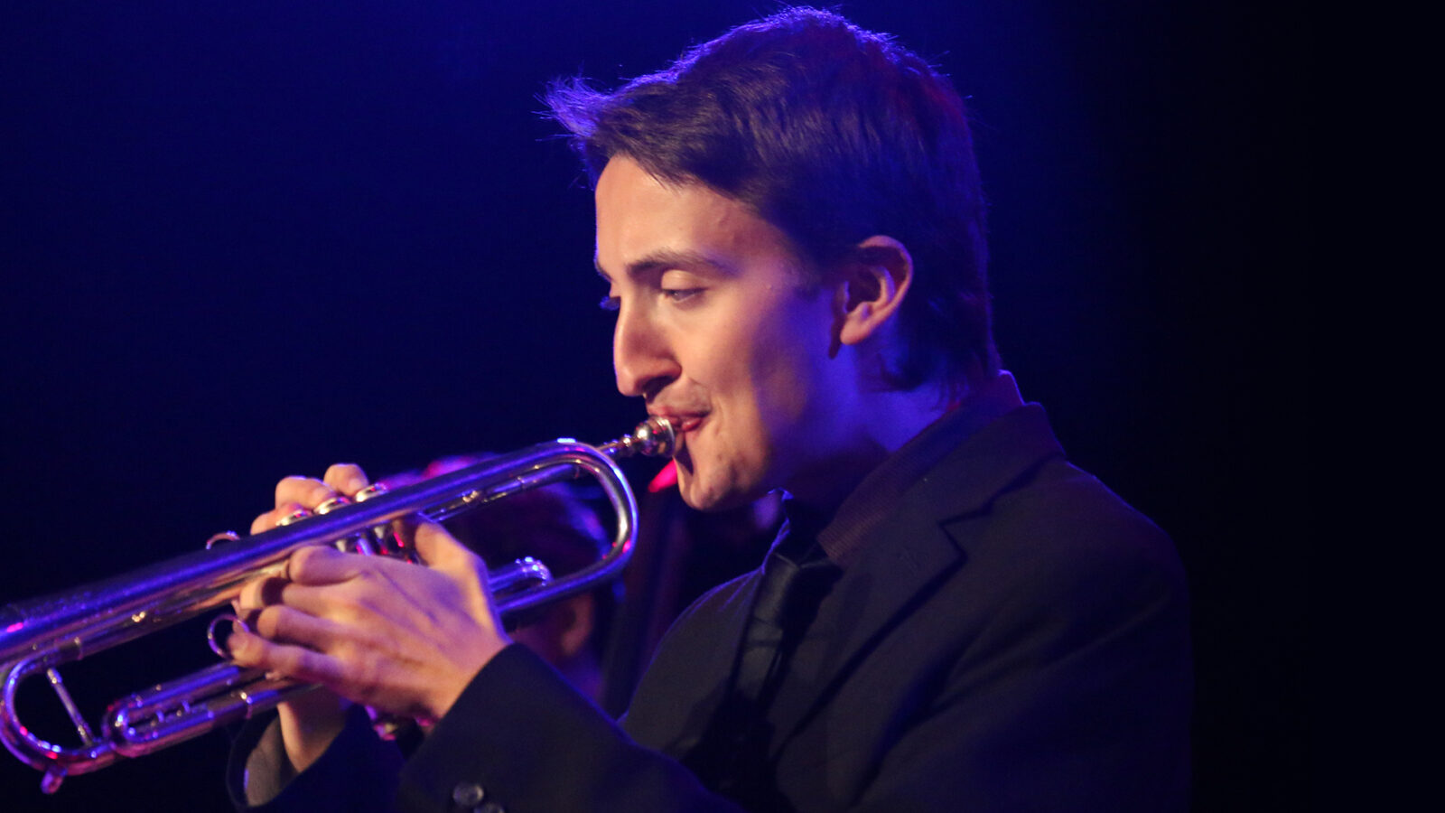 Photo of a trumpet player in purple stage light. 