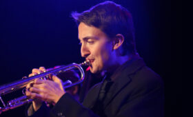 Photo of a trumpet player in purple stage light.