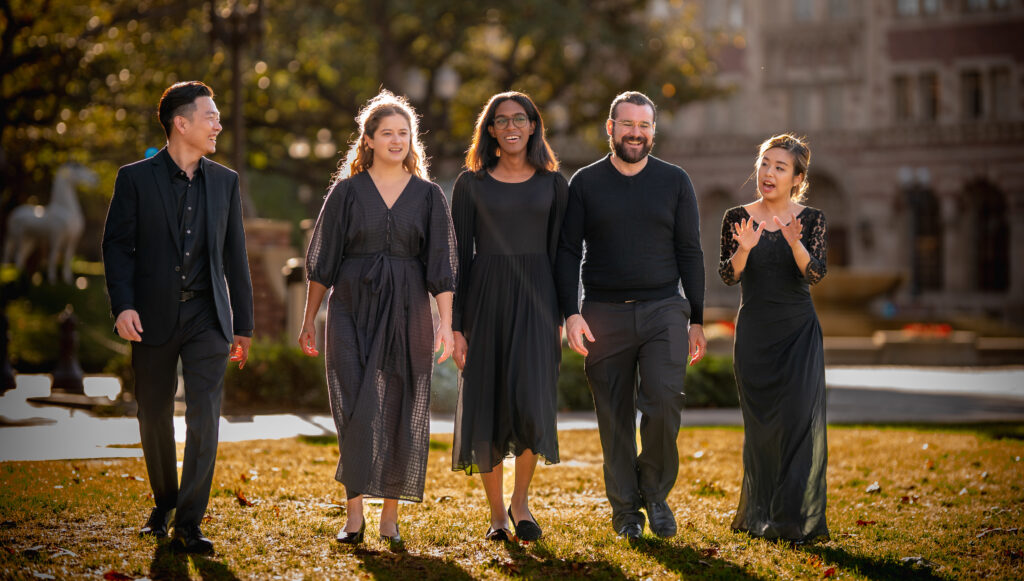 Choral students wearing black dress attire walk through the campus of a university laughing and smiling.