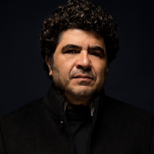 Photo of Otmaro Ruiz wearing a dark coat against a black background.