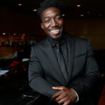 Photo of Paul Cornish smiling in a dark suit inside a piano bar.