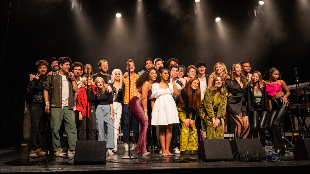 Group of popular music students smile together on stage after a concert.