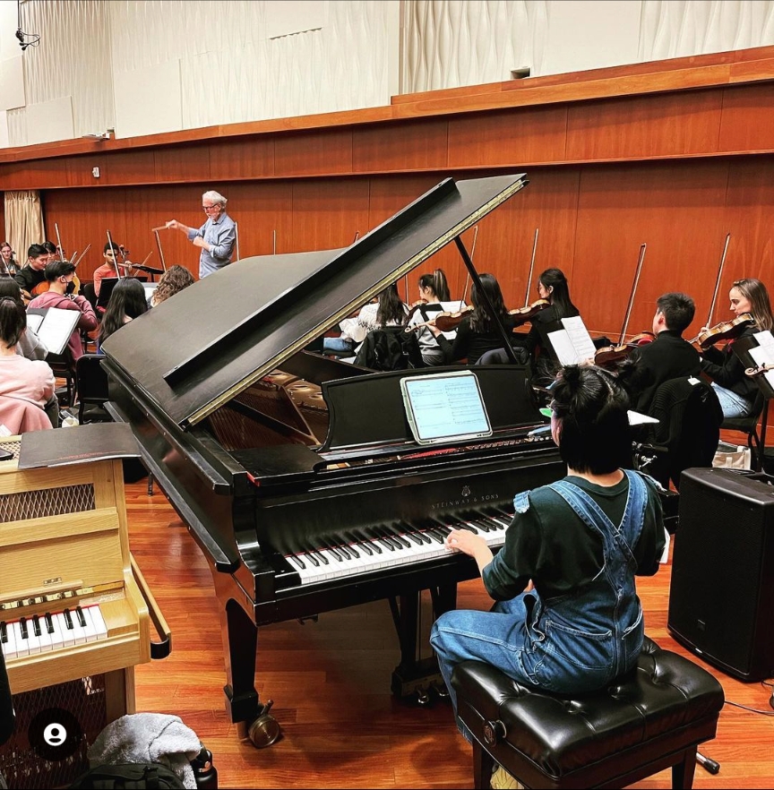 A pianist seated at the piano playing along with the USC Thornton Symphony in a rehearsal.