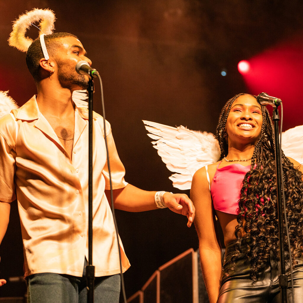 Two popular music performers wearing angel costumes smile on stage.
