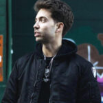 Tariq Cherif wearing a dark jacket in front of a painted green brick wall.