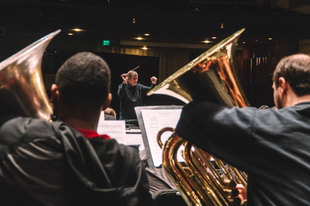 Conductor leads an orchestral wind ensemble on stage holding a baton.