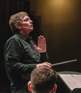 Conductor leads an orchestral wind ensemble on stage holding a baton.