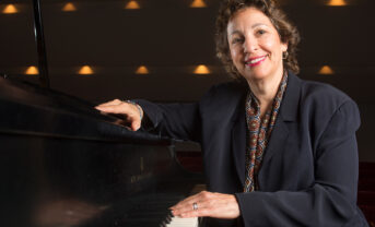 Photo of Iris Levine wearing a black dress seated at a piano.