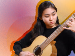 A classical guitarist plays her instrument in front of a brightly colored artistic background.