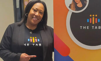 Photo of Angelica Brooks standing next to a colorful banner indoors.