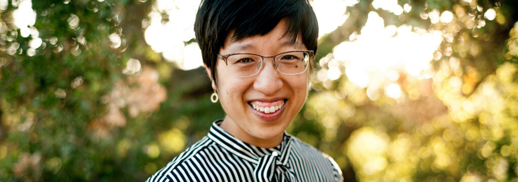 Photo of Emily Sung looking into the camera and smiling outside in the sunlight.