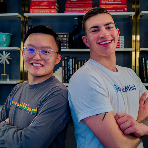 Photo of two smiling people in daylight in front of a bookshelf full of books.