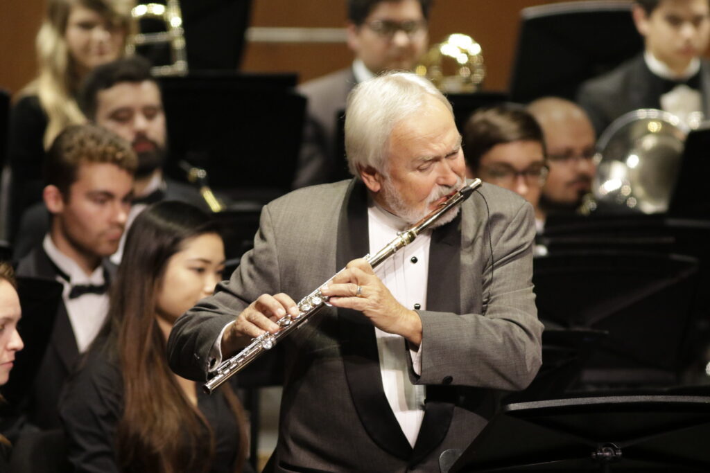 Photo of Jim Walker performing with his flute in concert attire on a classical performance stage.