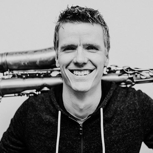 Saxophonist Derek Brown poses for the camera with his instrument behind him.