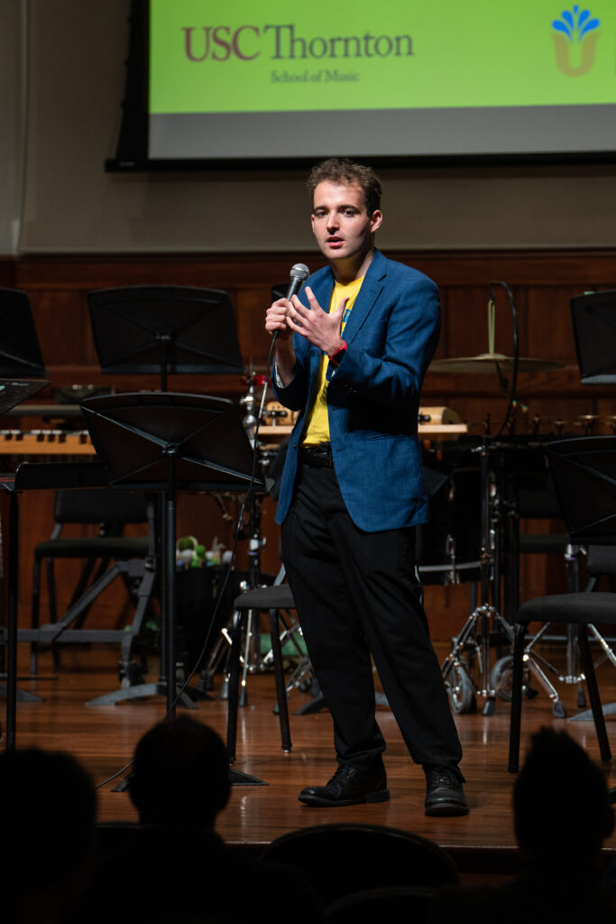 A music student gives a speech on stage in formal attire.