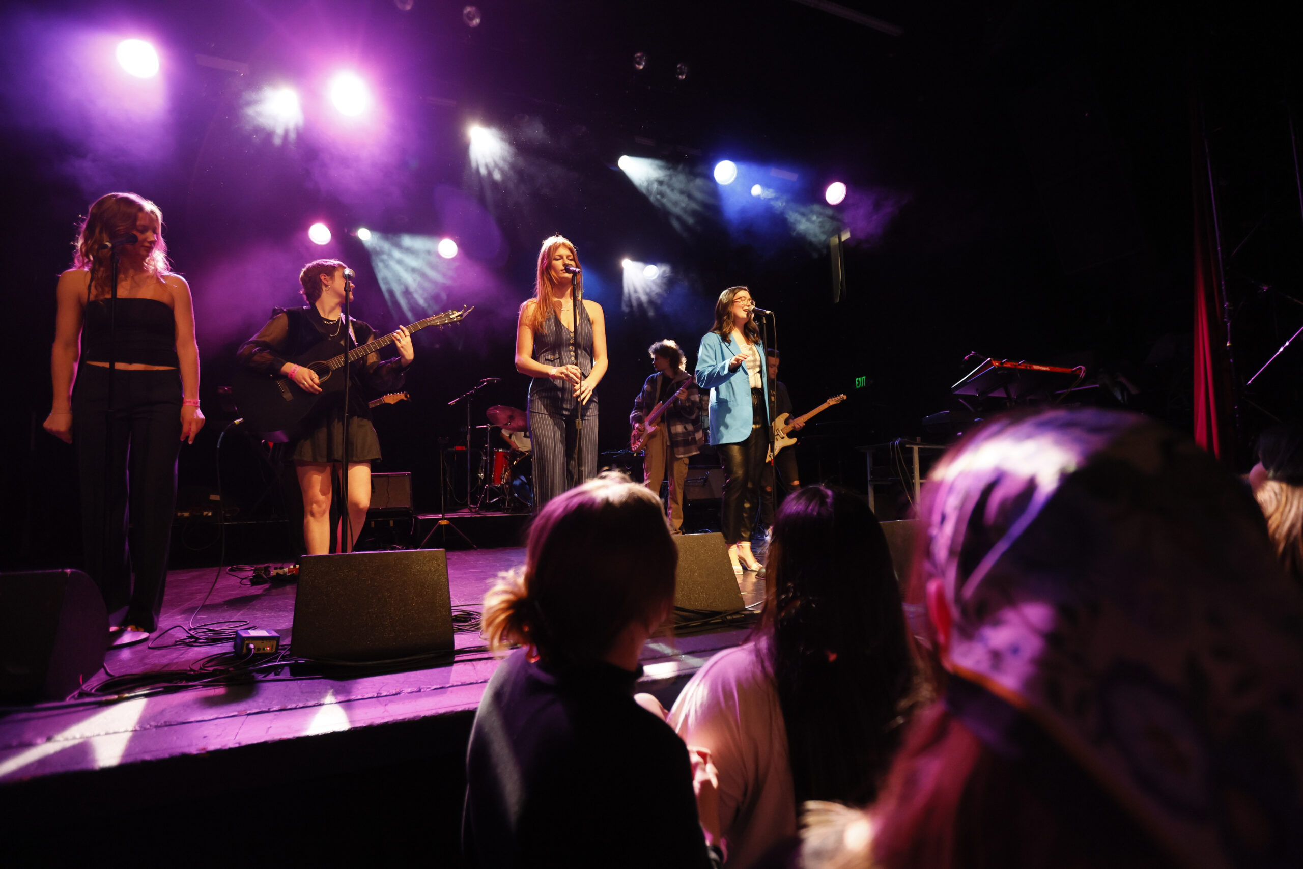 Students singing and playing onstage under colored lights for a crowd.