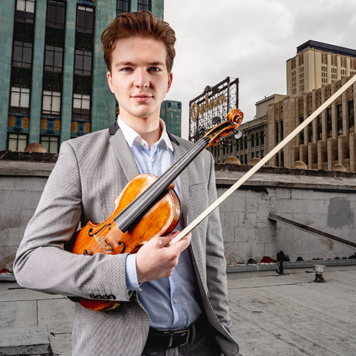 Photo of violinist Misha Vayman holding his instrument on a downtown rooftop.