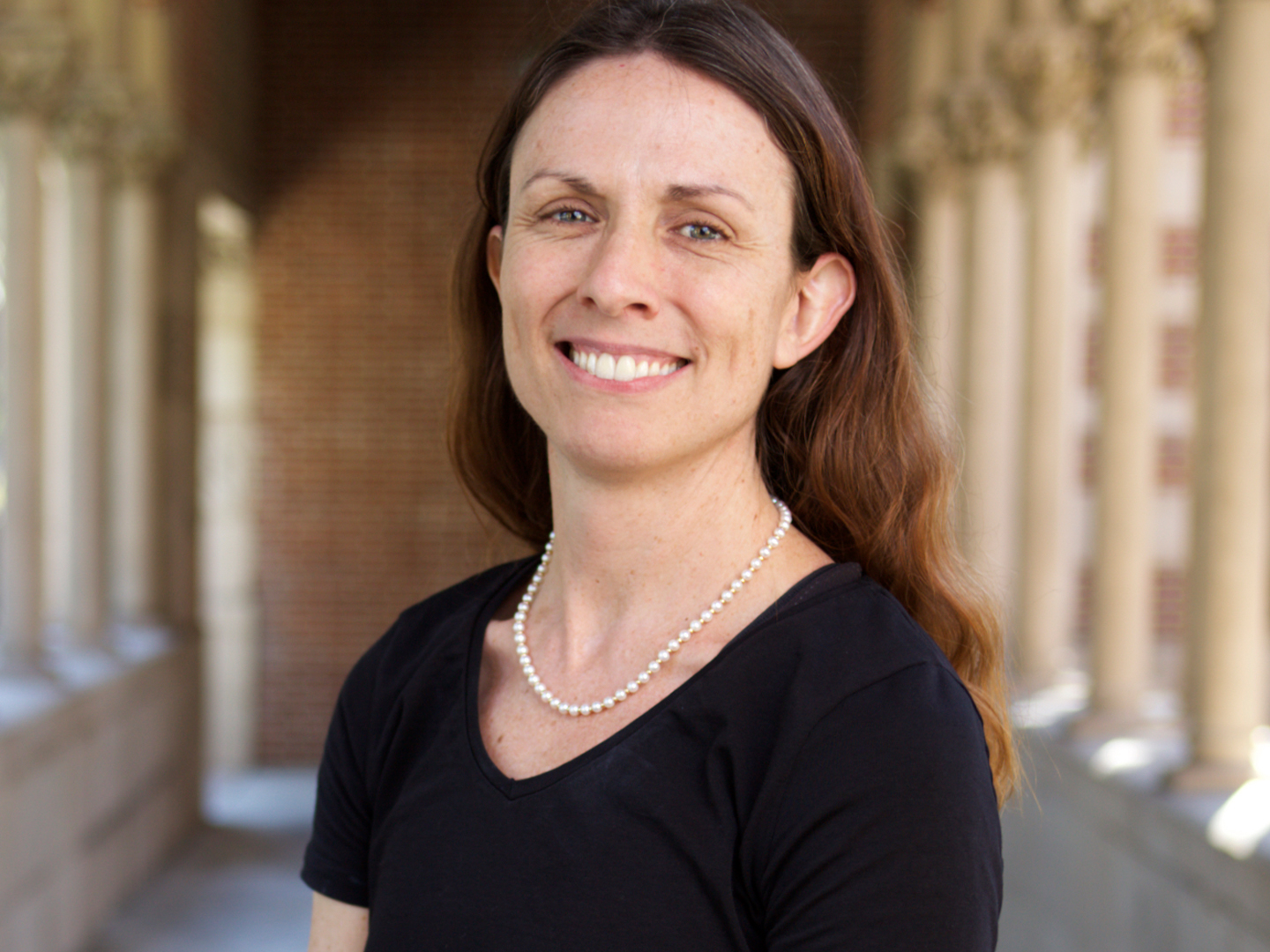 A female music instructor wearing a black blouse smiles outside near a library. 