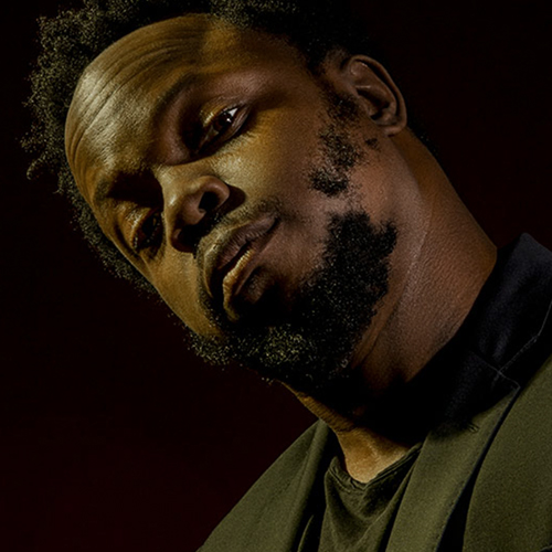 Trumpeter Ambrose Akinmusire looking into the camera in a dimly lit room.