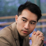 Concert pianist Rixiang Huang posing in front of a window indoors and looking off to the right of the camera.