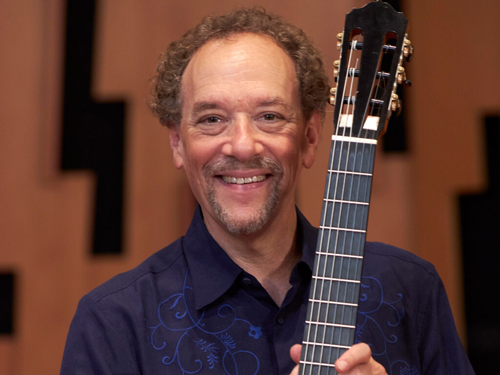 A classical guitarist holding a guitar and smiling.
