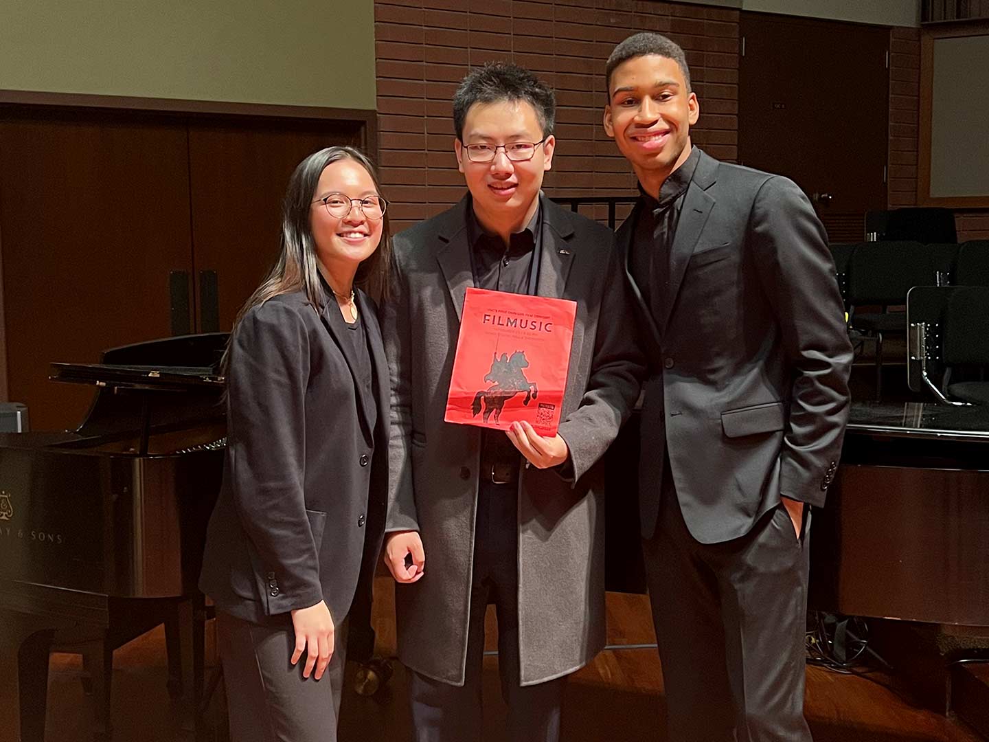 Photo of three smiling students wearing concert black attire after a concert. 