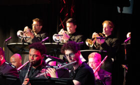 Jazz musicians on stage playing trumpets, horns and saxophones.