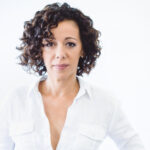 Luciana Souza wearing a white shirt looking into the camera in front of a white background.