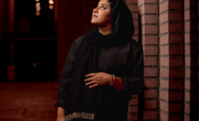 A singer wearing concert black attire and a headscarf looks away from the camera.