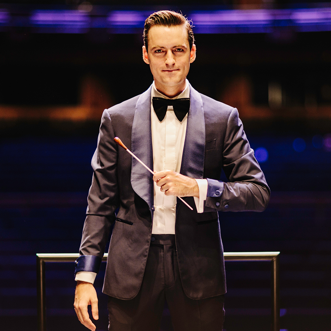 Composer Juan Pablo Contreras standing at a conductor's podium dressed in a concert suit.