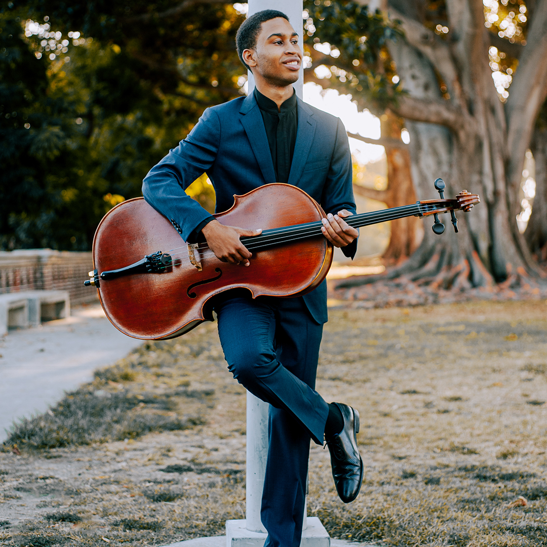 Cellist Quenton Blache holding his instrument and standing outside.