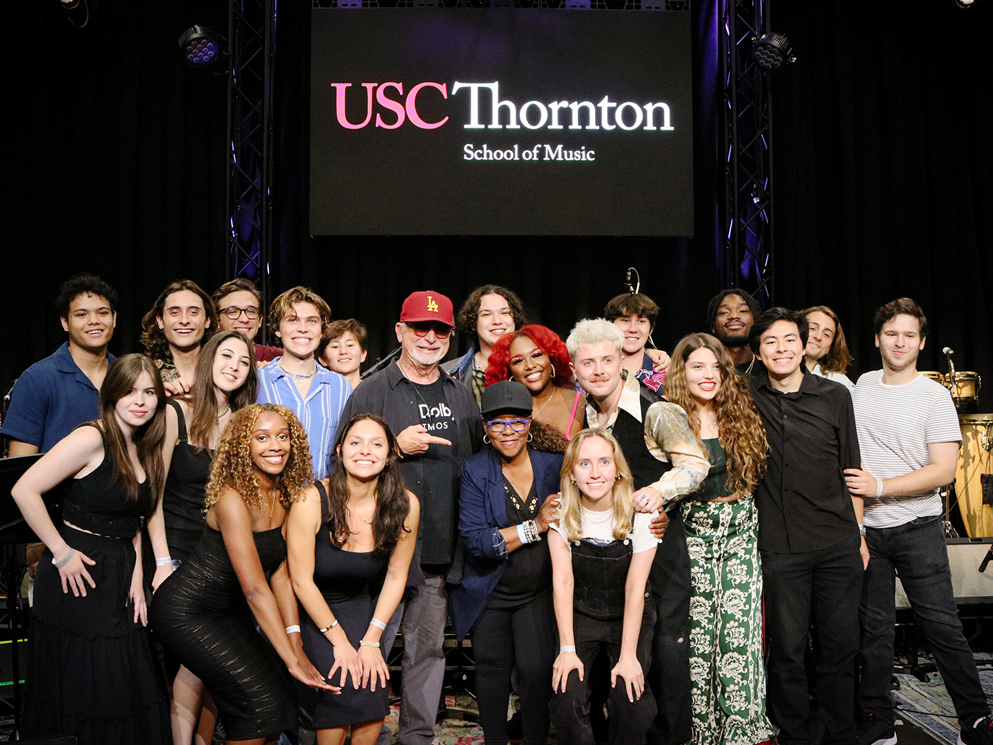 A group of popular music students gather together and smile on stage. 