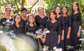 Ensemble of female singers pose for a photo in a garden.
