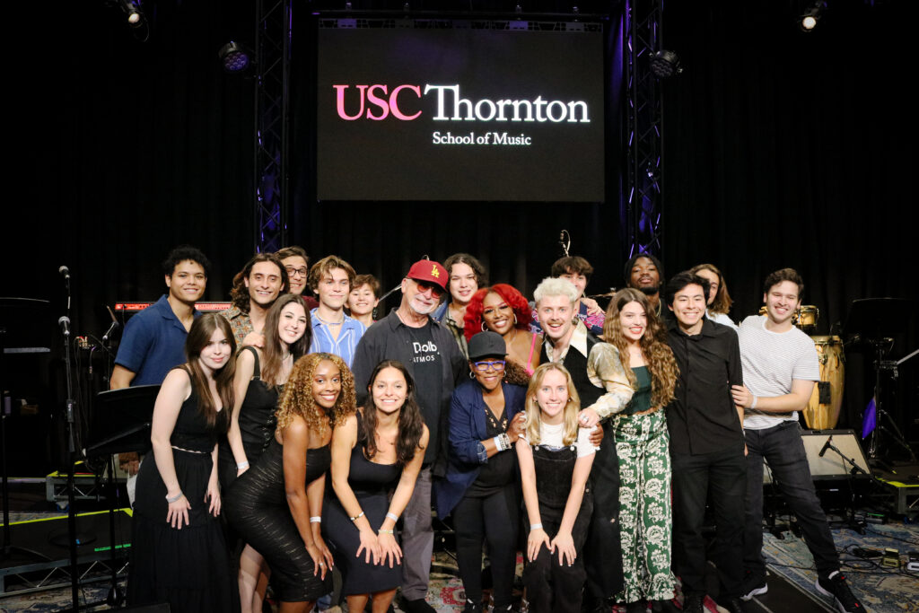 A group of popular music students gather together and smile on stage.