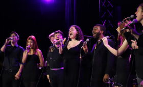 Vocal Jazz students performing on microphones onstage wearing concert attire.