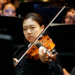 A violinist plays on stage in concert attire.